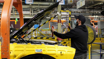 An operator at FCA's Brampton Assembly Plant installs a removable plexiglas partition in the engine compartment of a Dodge Challenger to help staff maintain social distancing against the coronavirus disease