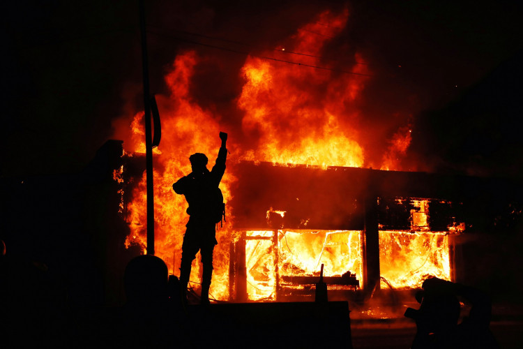 A protester gestures as buildings burn during continued demonstrations against the death in Minneapolis police custody of African-American man George Floyd