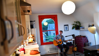 Musician Theo Bard sings as he performs an online gig from his kitchen in London