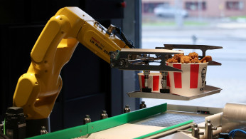 A robotic arm places a tray of food to a conveyor belt at a KFC restaurant offering contactless service