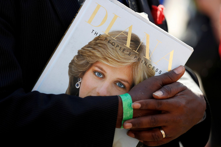 FILE PHOTO: A royal fan cradles a book about the late Princess Diana at the gates of her former residence in Kensington Palace on the twentieth anniversary of her death