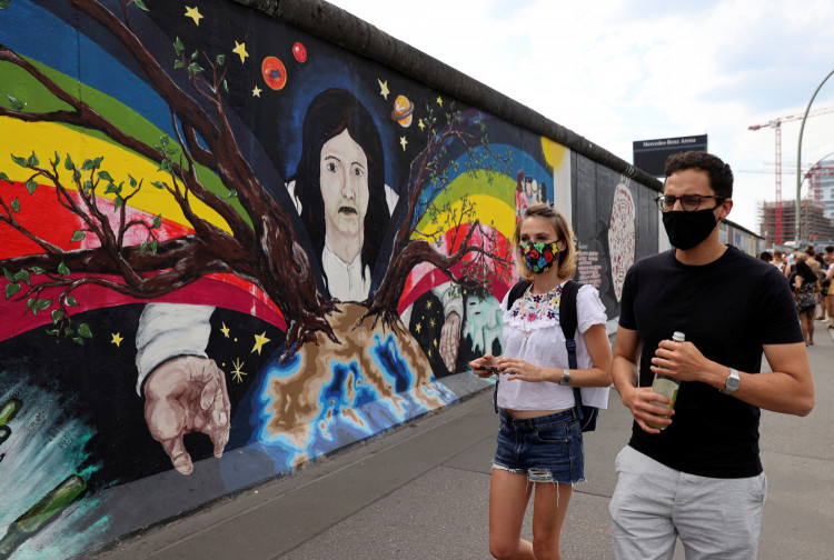Tourists from France wear face masks as they walk past the East Side Gallery,