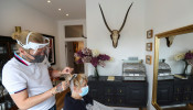 A hairstylist wearing a face shield works on the hair of the client Susan Hepple at the Hair by Reiss salon