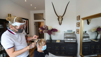 A hairstylist wearing a face shield works on the hair of the client Susan Hepple at the Hair by Reiss salon