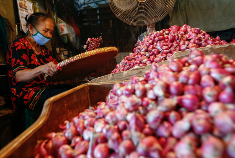 A worker wearing a protective face mask sorts onion