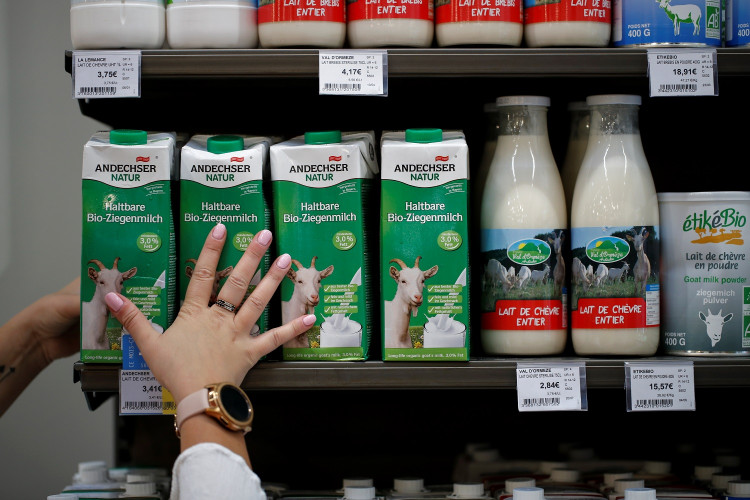 An employee prepares goat's milk cartons as she restocks a sales display