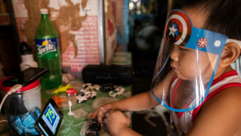A boy wears a face shield while watching a simulation of an online learning class