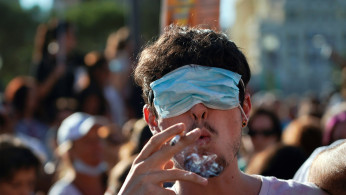 A man smokes a cigarette with his eyes covered by a face mask as he takes part in a protest against the use of protective masks during the coronavirus disease pandemic