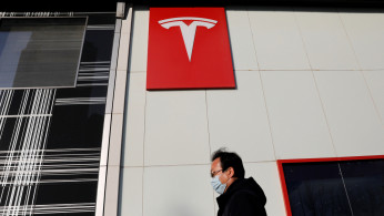 Man wearing a face mask walks past the electric vehicle maker Tesla's showroom in Beijing