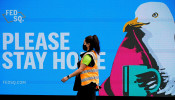FILE PHOTO: An essential worker walks past a 'Please Stay Home' sign 
