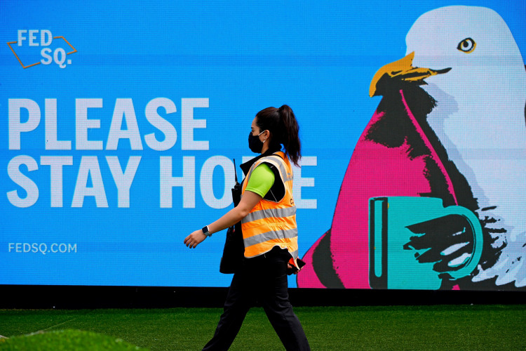 FILE PHOTO: An essential worker walks past a 'Please Stay Home' sign 