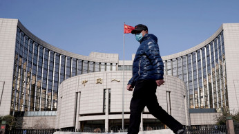 A man wearing a mask walks past the headquarters of the People's Bank of China.