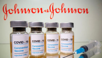 Vials with a sticker reading, 'COVID-19' are seen in front of a displayed Johnson & Johnson logo.