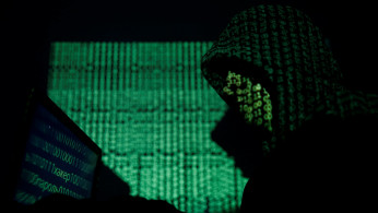 A hooded man holds a laptop computer as cyber code is projected on him in this illustration picture taken on May 13, 2017. 