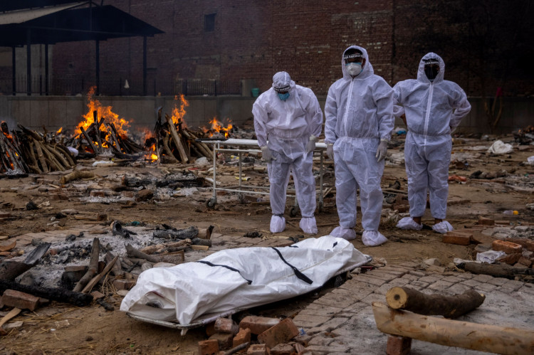 Men wearing protective suits stand next to the body of their relative, who died from the coronavirus disease (COVID-19), before her cremation at a crematorium ground in New Delhi, India, May 4, 2021. 