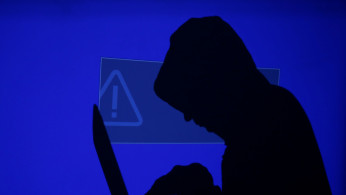 FILE PHOTO: A hooded man holds a laptop computer as blue screen with an exclamation mark is projected on him in this illustration picture taken on May 13, 2017. 