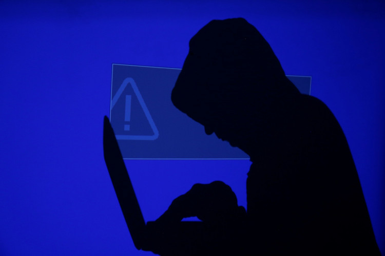 FILE PHOTO: A hooded man holds a laptop computer as blue screen with an exclamation mark is projected on him in this illustration picture taken on May 13, 2017. 