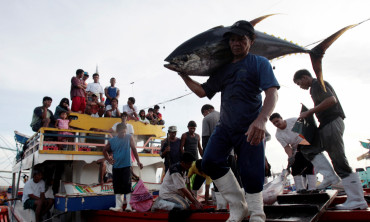 Fishermen and their families watch as a worker carries a yellow fin tuna off a fishing boat at fish at a port in General Santos City, Mindanao, southern Philippines January 10, 2008. 