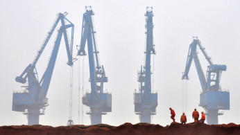 Workers remove the cloth covering the iron ore from Australia while they prepare for transporting at a port in Tianjin municipality