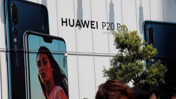 People walk past an advertisement for Huawei outside an electronic store in Tokyo