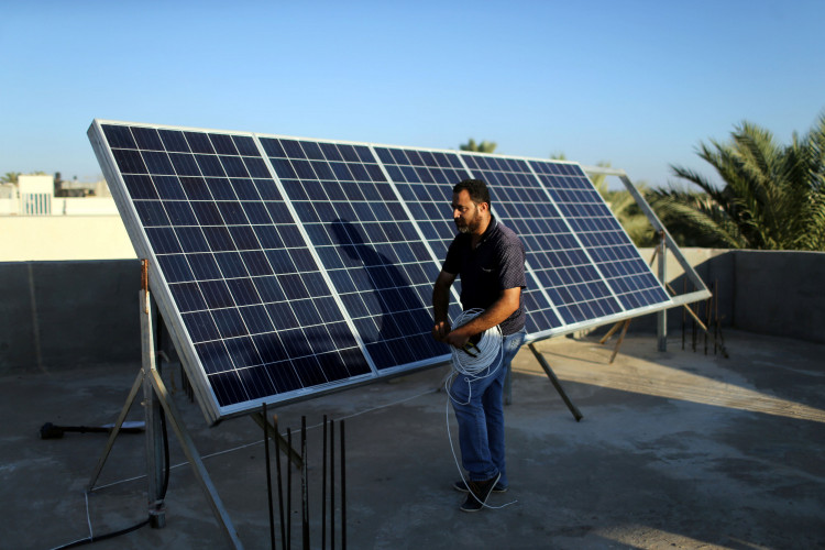 Palestinian man installs solar panels on a house rooftop in Khan Younis in the southern Gaza Strip