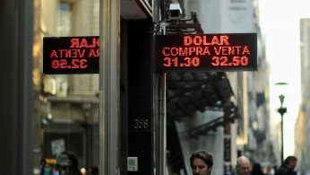 People walk past an electronic board showing currency exchange rates in Buenos Aires' financial district,