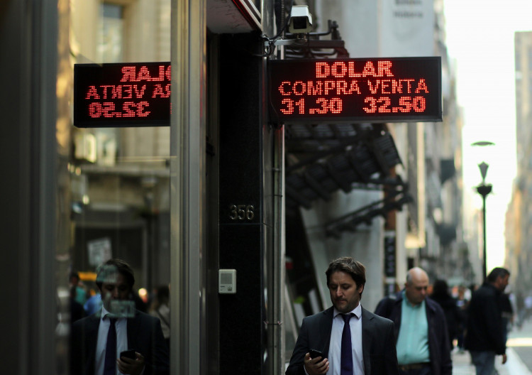 People walk past an electronic board showing currency exchange rates in Buenos Aires' financial district,