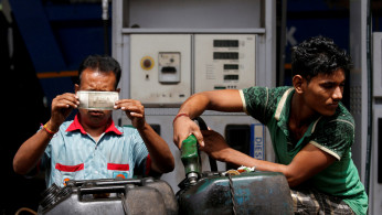 A worker checks a 500 Indian rupee note as a man fills diesel in containers at a fuel station in Kolkata