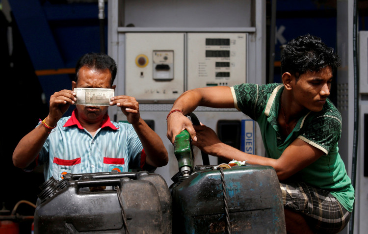 A worker checks a 500 Indian rupee note as a man fills diesel in containers at a fuel station in Kolkata