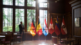 A security staff member stands next to the flags of Germany, Belgium, Luxembourg, Switzerland, Liechtenstein and Austria