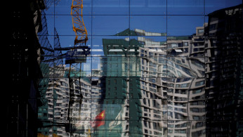 A construction site and a residential building are reflected on the glass wall of a building