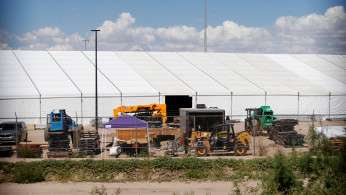 Construction equipment is seen at a tent encampment through a border fence near the U.S. Customs and Border Protection