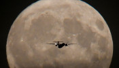 A passenger plane is seen with the full moon behind as it begins its final landing approach to Heathrow Airport in London