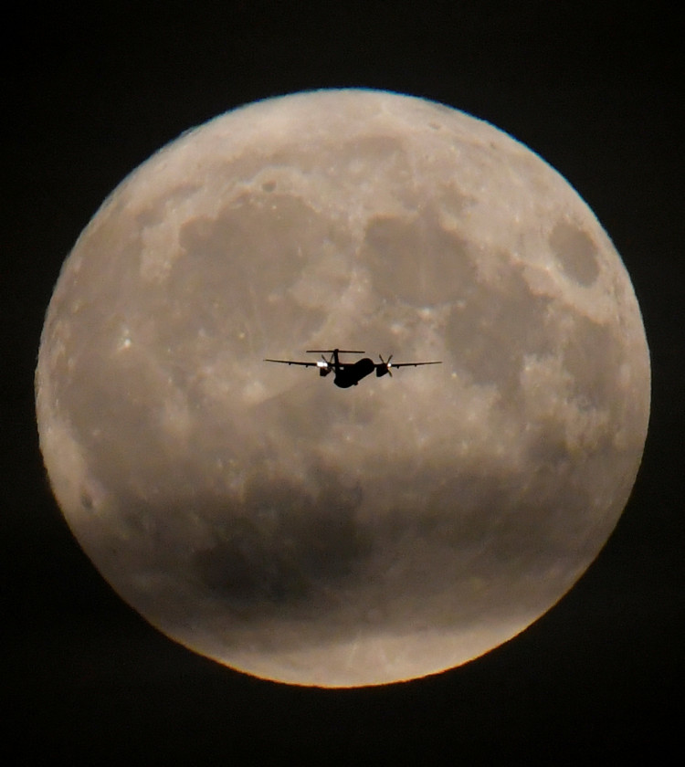 A passenger plane is seen with the full moon behind as it begins its final landing approach to Heathrow Airport in London