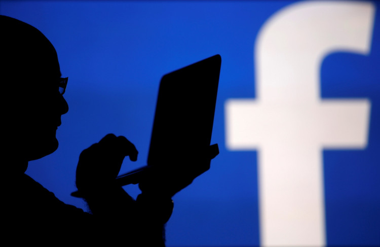A man is silhouetted against a video screen with an Facebook logo in this photo illustration in Zenica