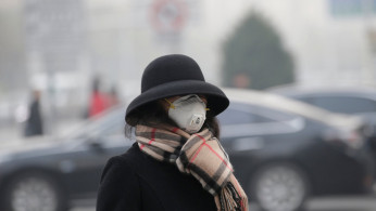 A woman wearing a mask walks on a road as heavy smog blankets China's capital Beijing