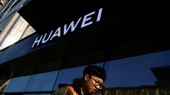A man uses his phone as he walks past a Huawei shop in Beijing