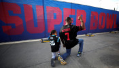 Anar Kahn, wearing a Colin Kaepernick football jersey kneels with his young son outside Mercedes Benz Stadium in Atlanta