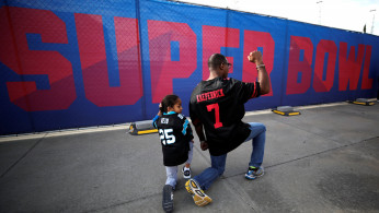 Anar Kahn, wearing a Colin Kaepernick football jersey kneels with his young son outside Mercedes Benz Stadium in Atlanta