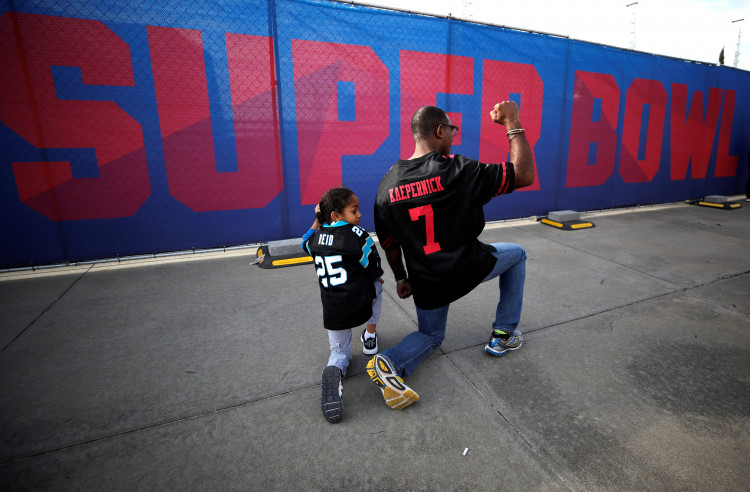 Anar Kahn, wearing a Colin Kaepernick football jersey kneels with his young son outside Mercedes Benz Stadium in Atlanta