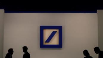 People are silhouetted next to the Deutsche Bank's logo prior to the bank's annual meeting in Frankfurt