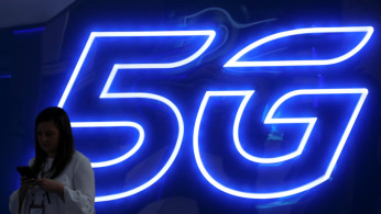 A woman looks at her mobile phone next to a 5G sign at the Mobile World Congress in Barcelona