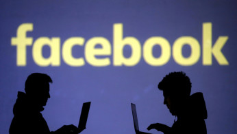  Silhouettes of laptop users are seen next to a screen projection of Facebook logo in this picture illustration