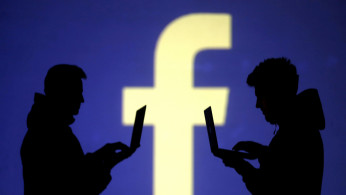 FILE PHOTO: Silhouettes of laptop users are seen next to a screen projection of Facebook logo in this picture illustration