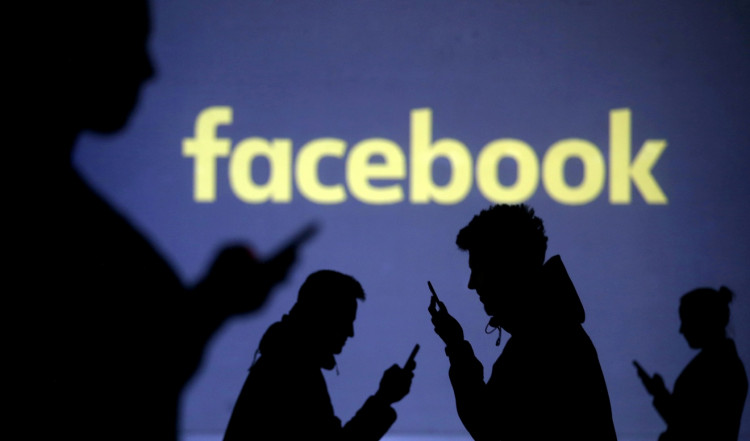 Silhouettes of mobile users are seen next to a screen projection of Facebook logo in this picture illustration