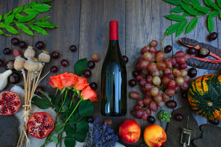 Wine bottle beside grapes roses and several fruits on brown wooden surface