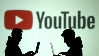 Silhouettes of mobile device users are seen next to a screen projection of Youtube logo in this picture illustration