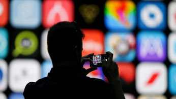 A visitor uses his iPhone X to take photos of the stage at the Apple Worldwide Developer conference (WWDC) in San Jose