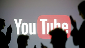 People pose with mobile devices in front of projection of Youtube logo in this picture illustration taken in Zenica