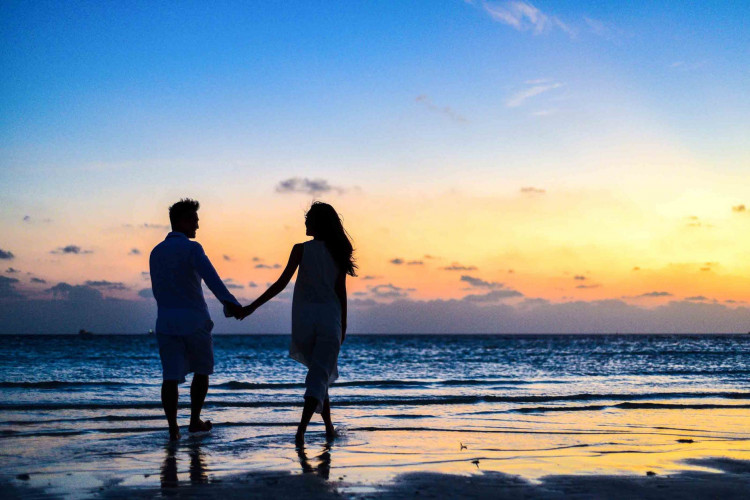 Man and woman holding hands beside the sea.